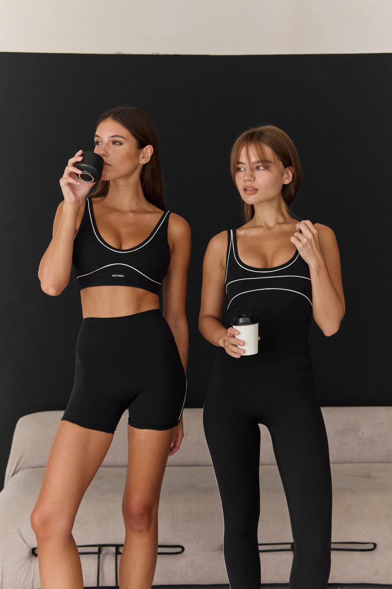 Two women in black athletic wear standing in a room with a black wall and beige couch.