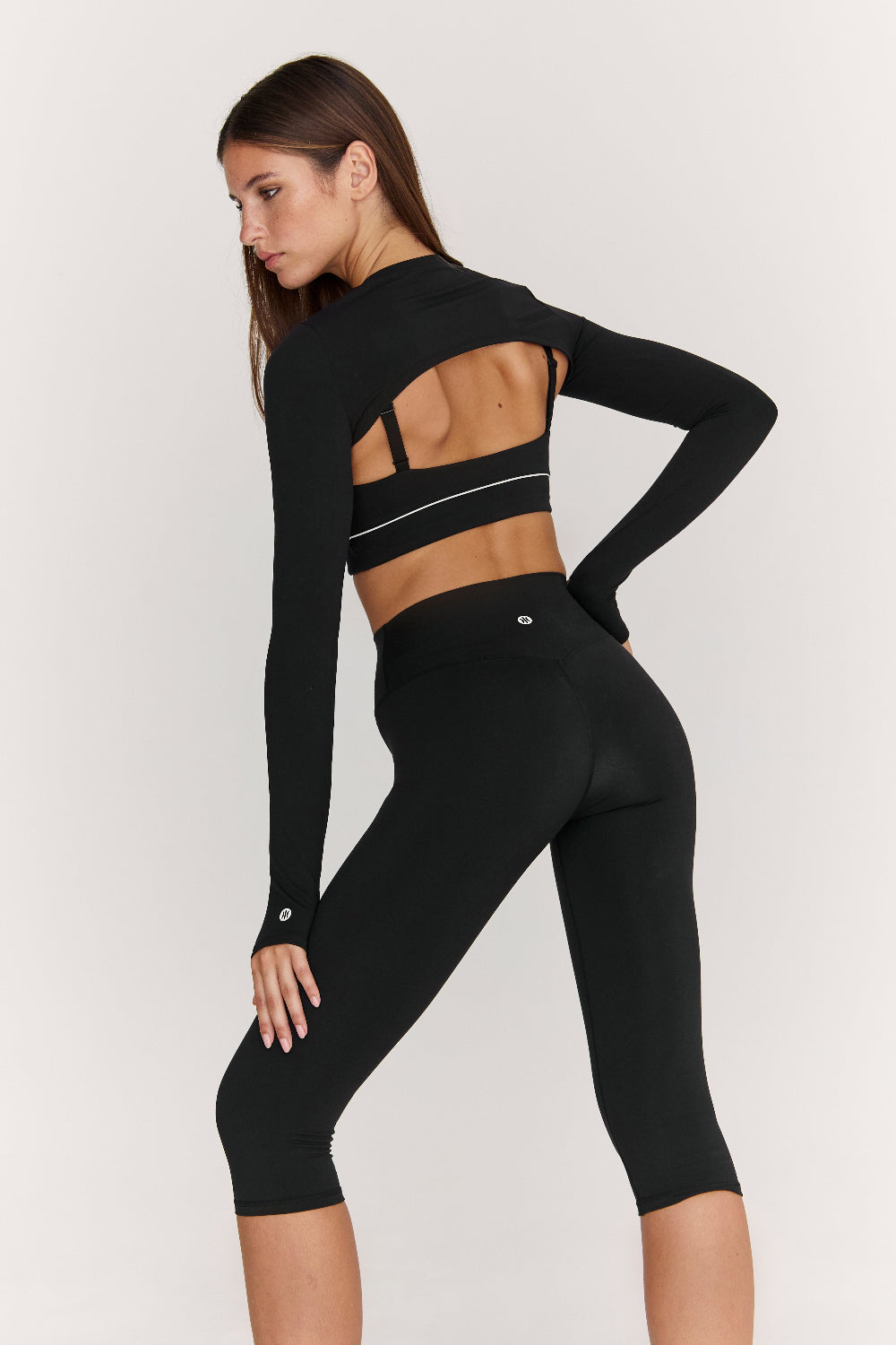 Person wearing a black long-sleeve crop top and leggings on a white background