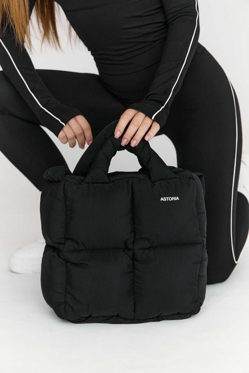 Person holding a black bag with 'ASTORIA' branding on a white background