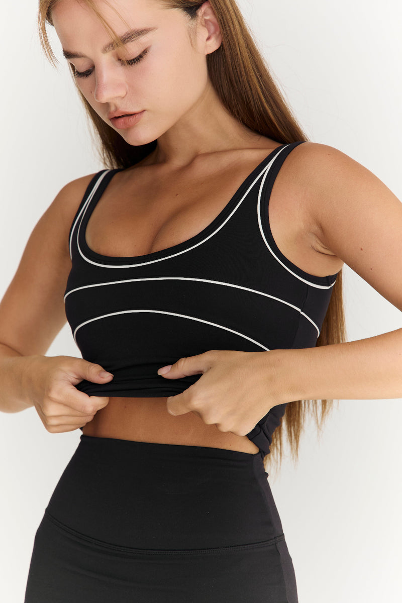 Woman wearing a black sports bra with white straps on a plain background