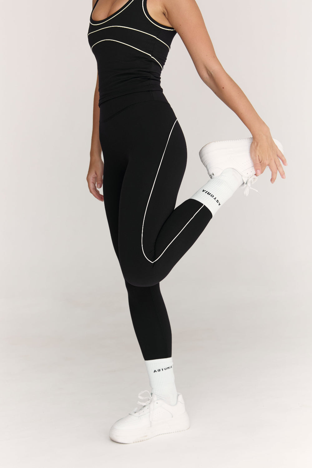 Person wearing black athletic leggings with white accents on a plain background