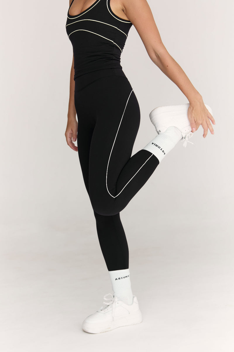 Person wearing black athletic leggings with white accents on a plain background